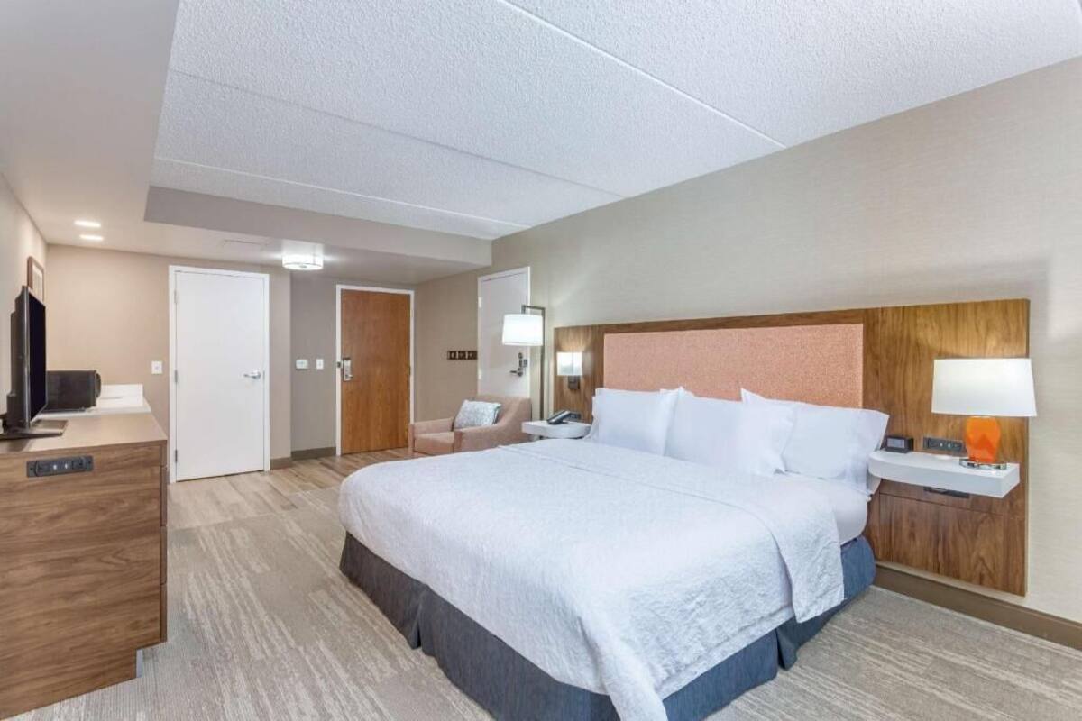A hotel room with a large bed, a desk, a chair, a TV, and a bathroom door.