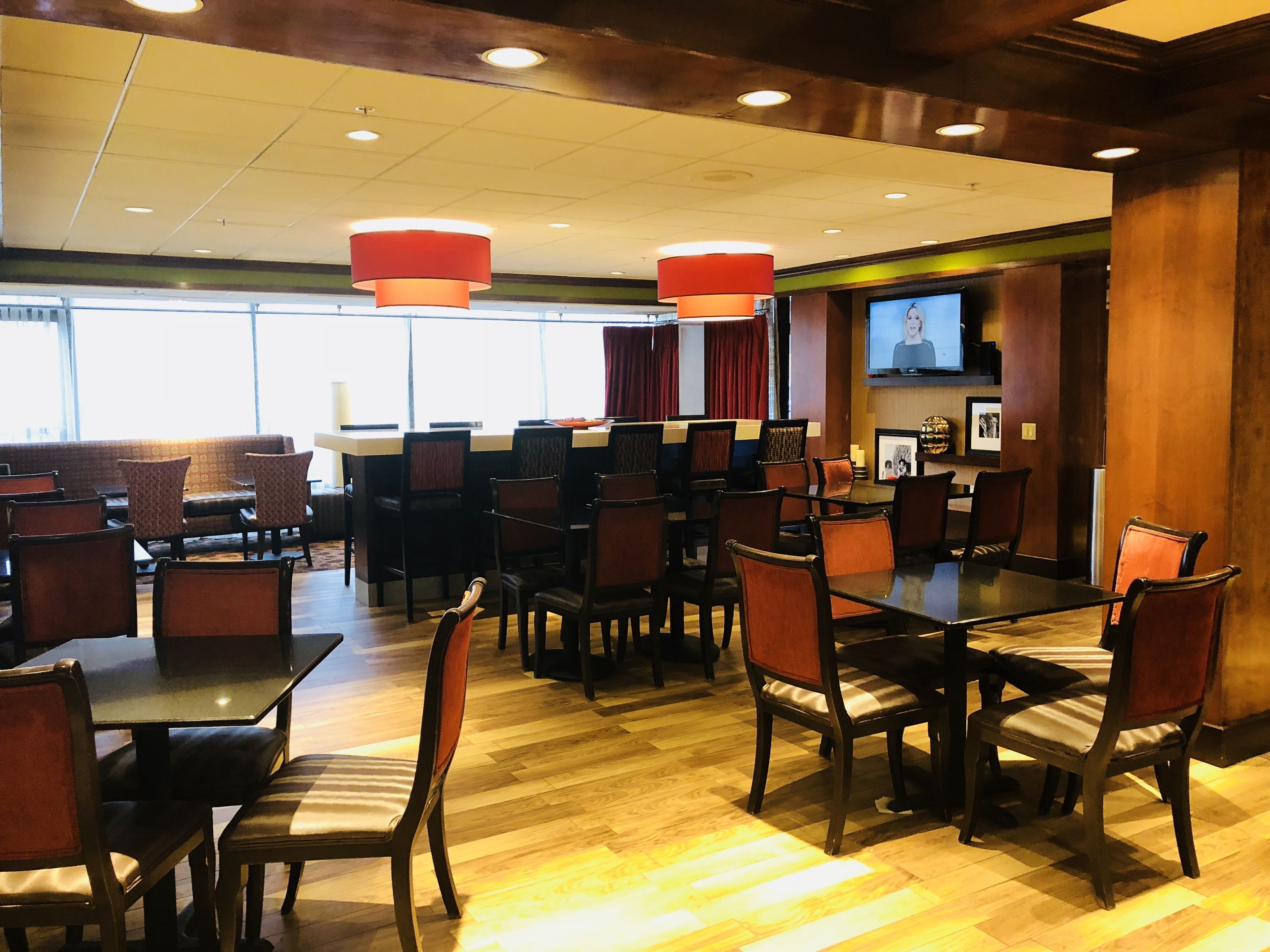 Un comedor de hotel con varias mesas y sillas, un bar y una pantalla de televisión.