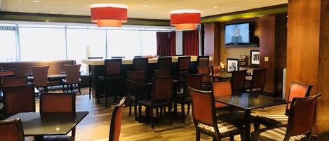 Un comedor de hotel con varias mesas y sillas, un bar y una pantalla de televisión.