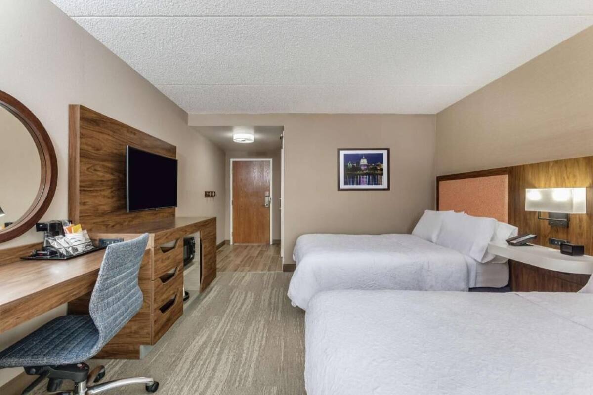 A hotel room with a desk, two beds, a TV, and a door leading to another room.