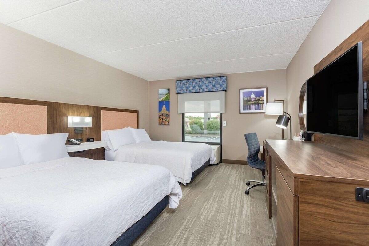 A hotel room with two beds, a desk, a chair, a TV, and a window with a view.