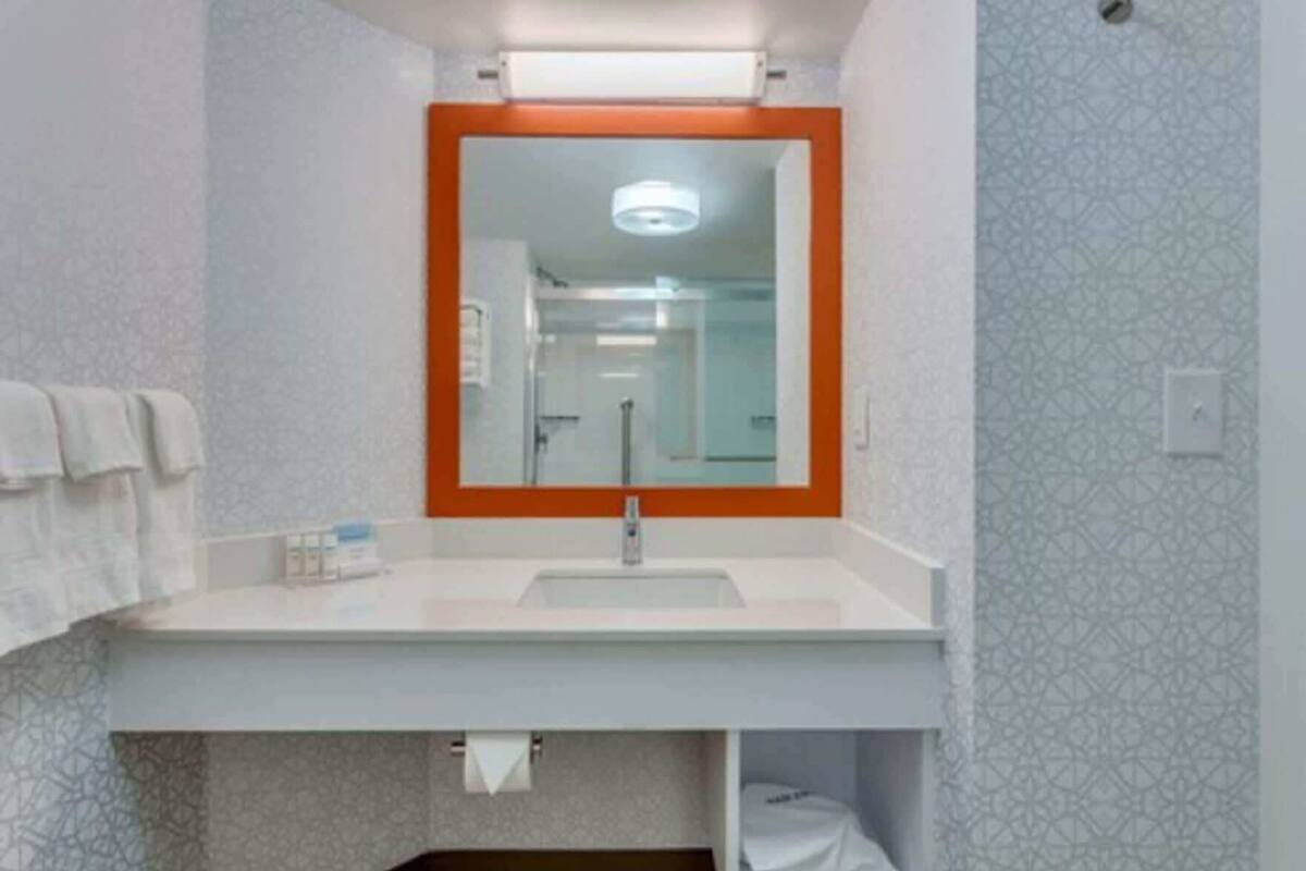 A bathroom with a white sink, a mirror with an orange frame, and patterned walls.