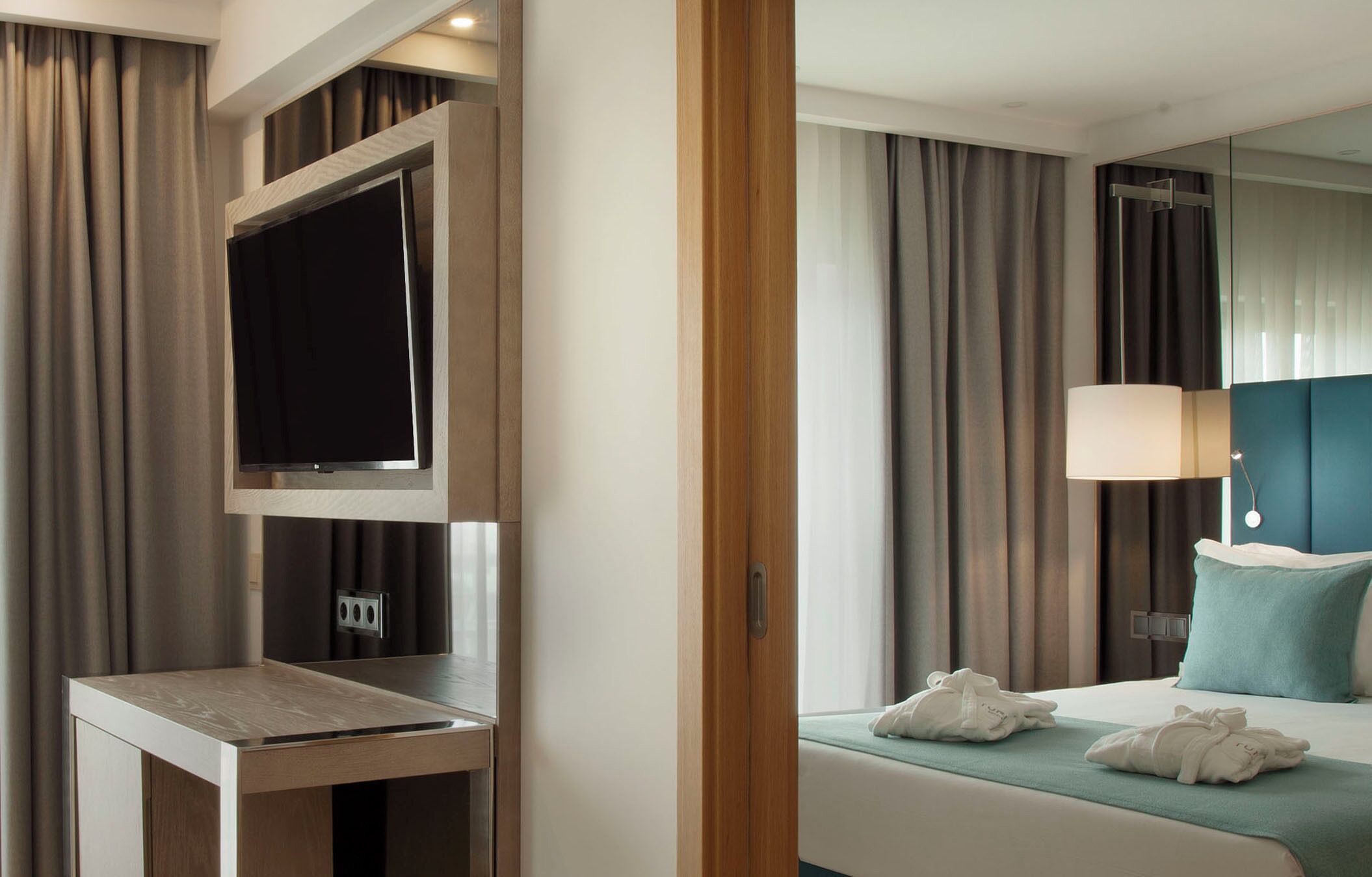 Una habitación de hotel con cama, mesita de noche, televisor y espejo.