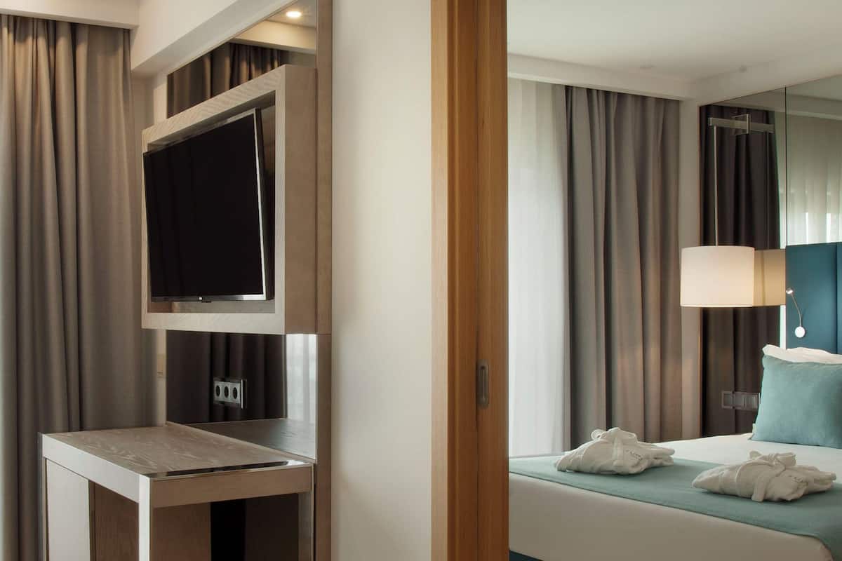 Quarto de hotel com cama, mesa de cabeceira, televisão e espelho.