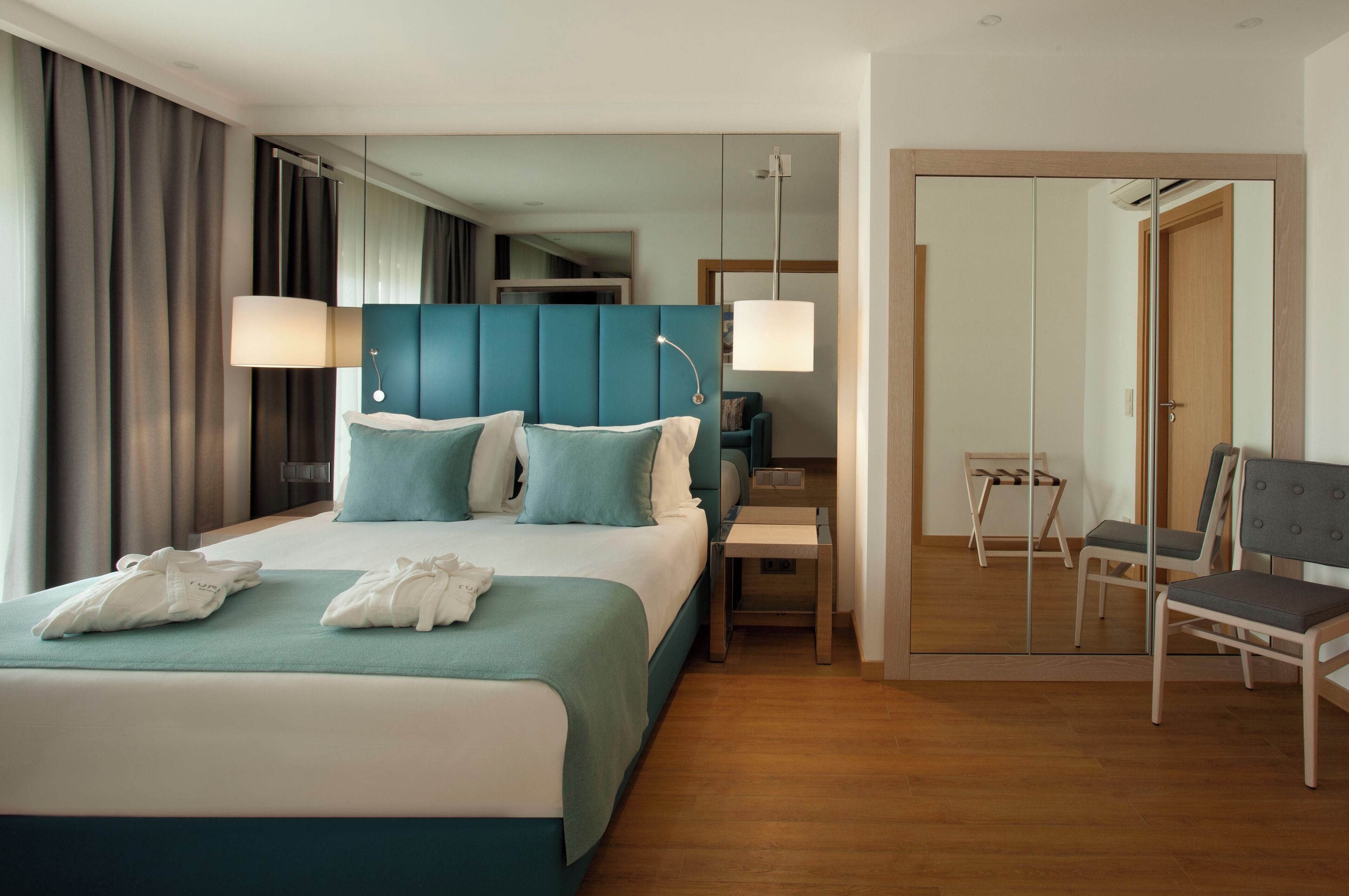 Una habitación de hotel moderna con una cama grande, mesitas de noche, una silla y un espejo.