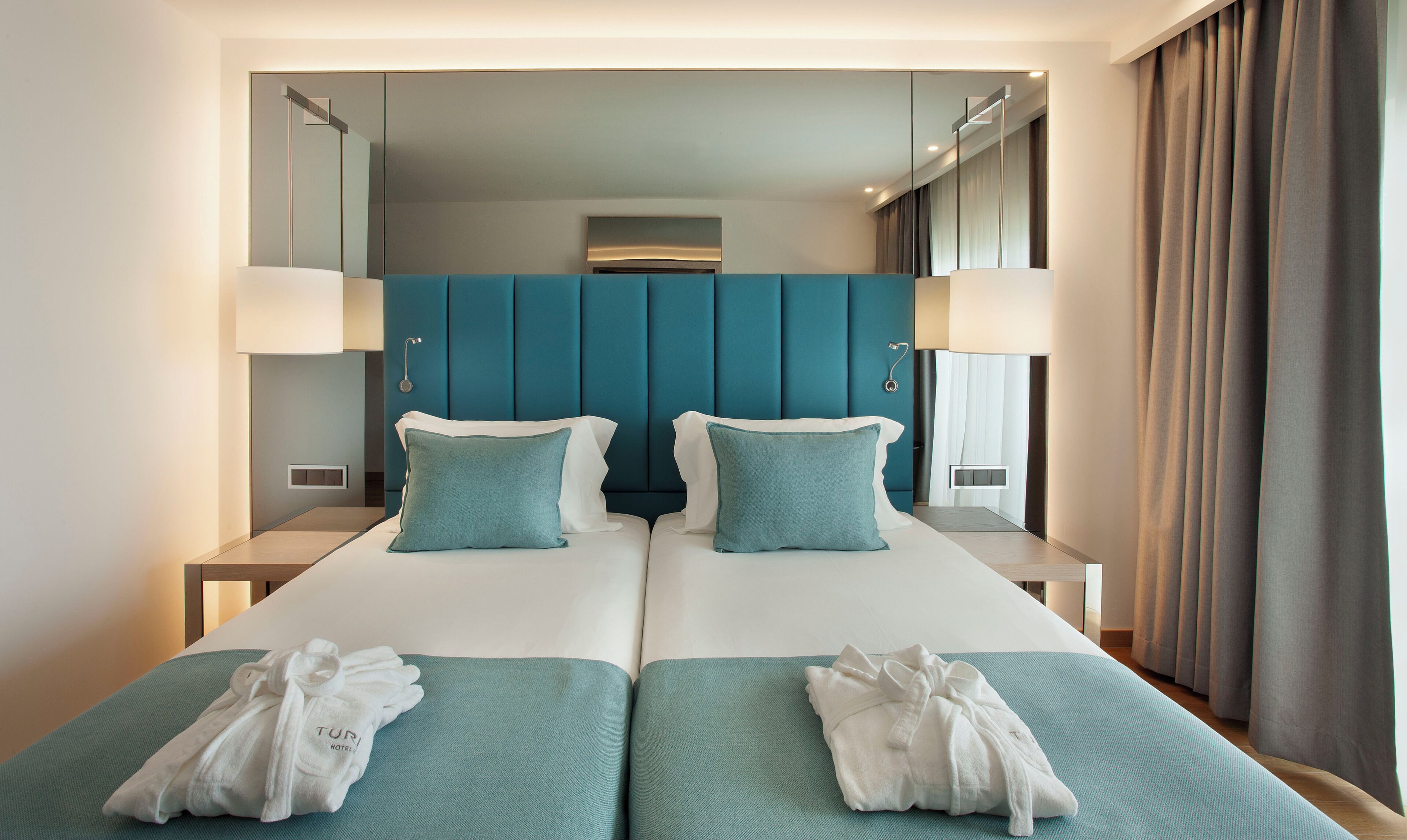 Una habitación de hotel moderna con una cama grande, dos mesitas de noche y un cabecero.