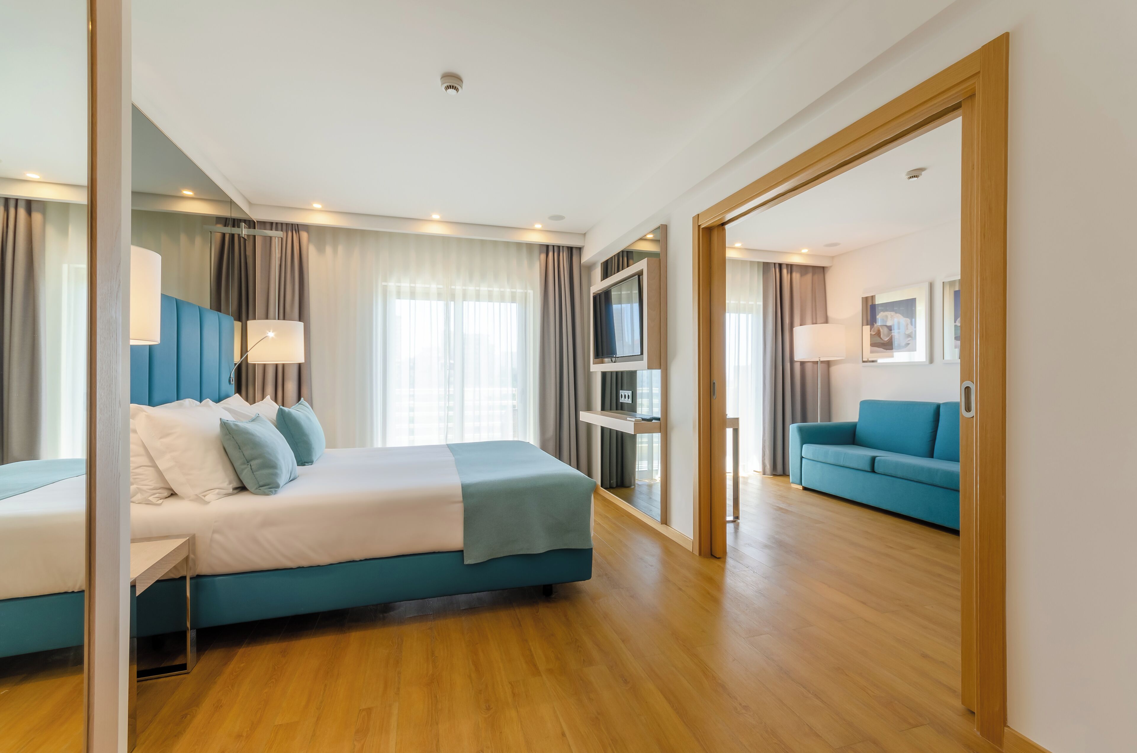Una habitación de hotel moderna con una cama grande, un sofá azul y un televisor sobre un soporte.