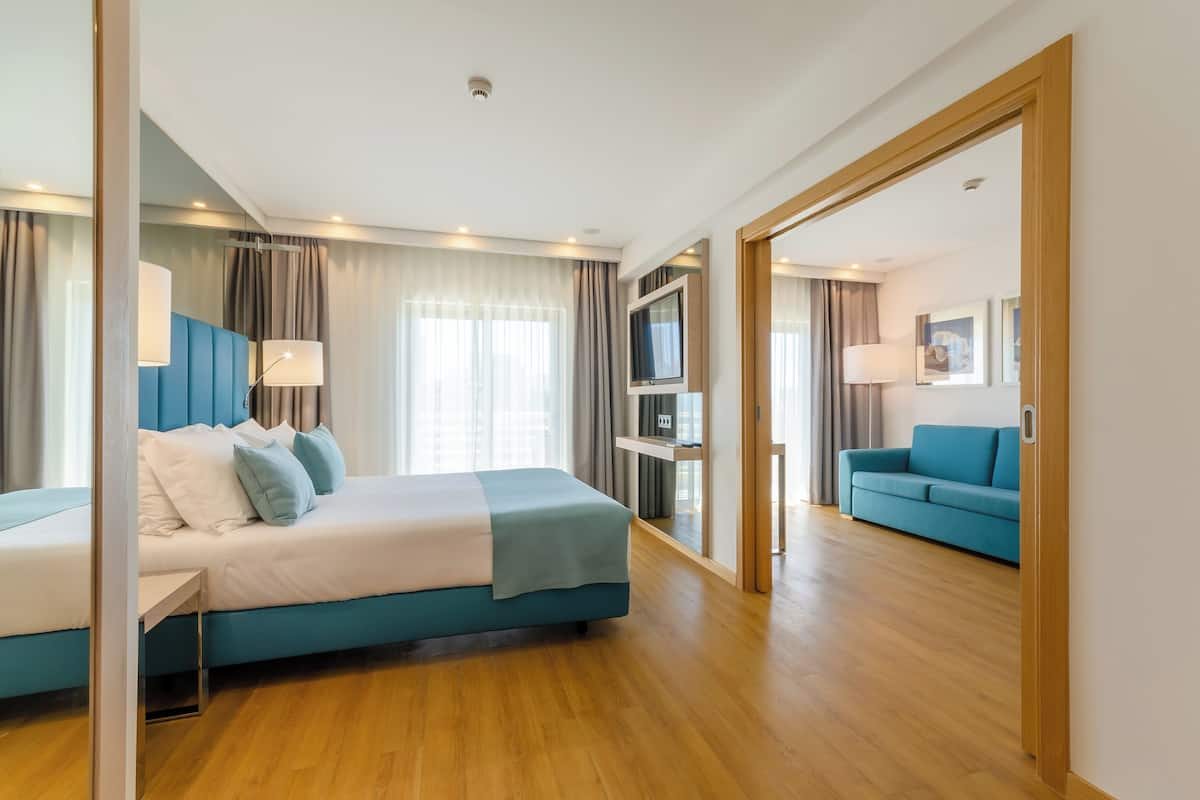 Quarto de hotel moderno com uma cama grande, um sofá azul e uma TV em um suporte.