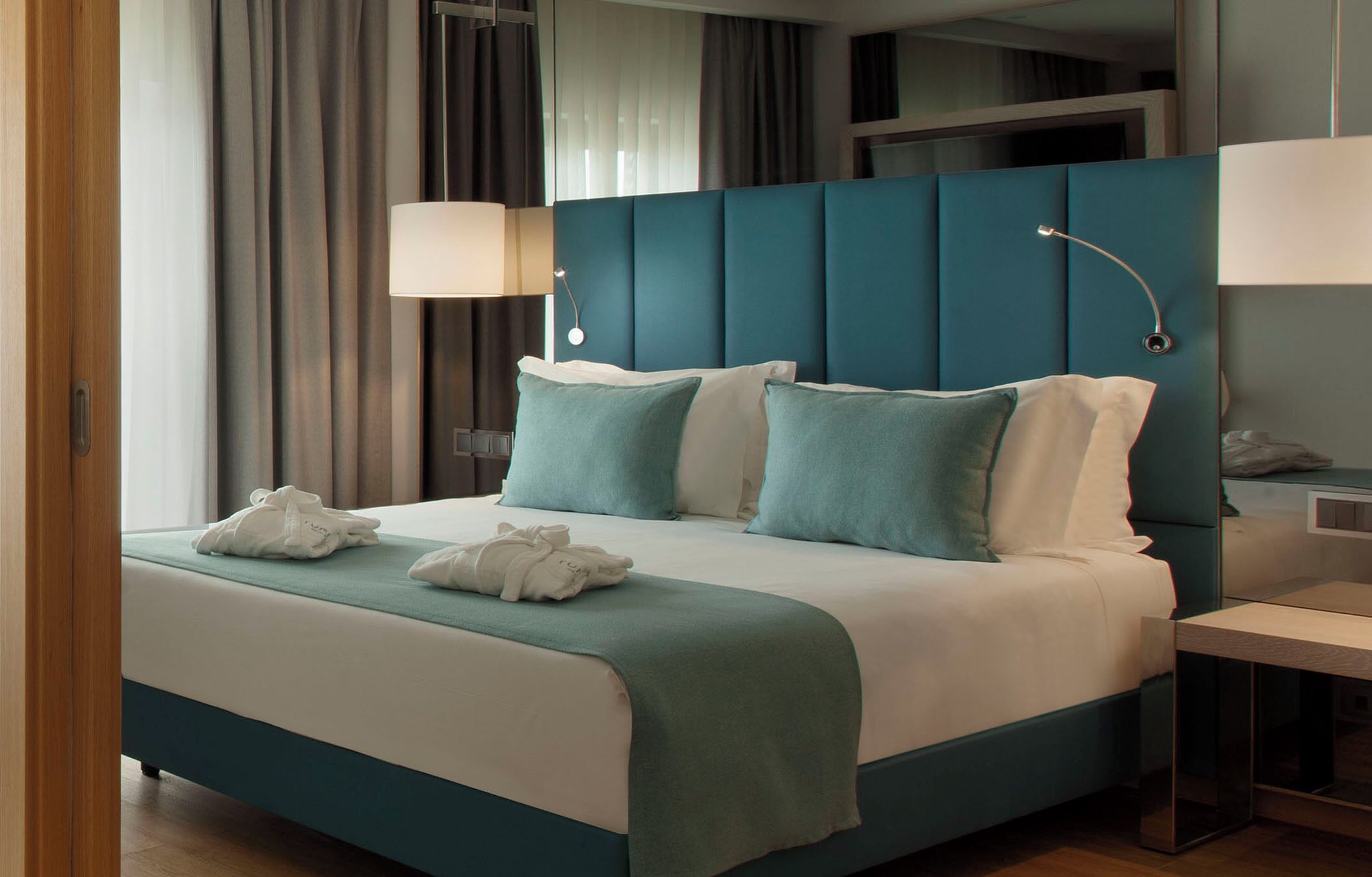 Habitación de hotel moderna con una cama grande, dos lámparas de noche y vistas de la ciudad a través del ventanal.