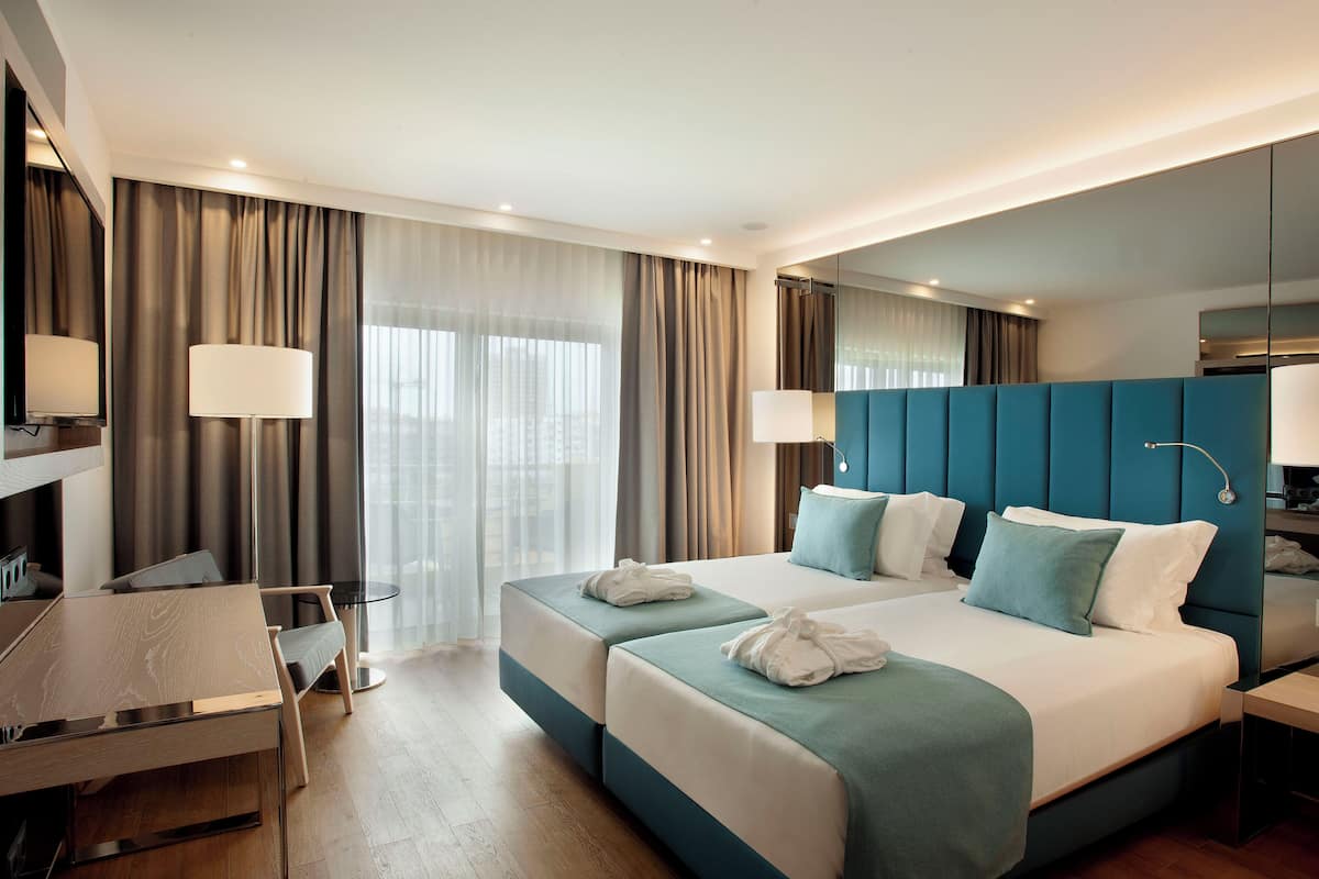 Quarto de hotel moderno com duas camas, uma escrivaninha e uma cadeira.