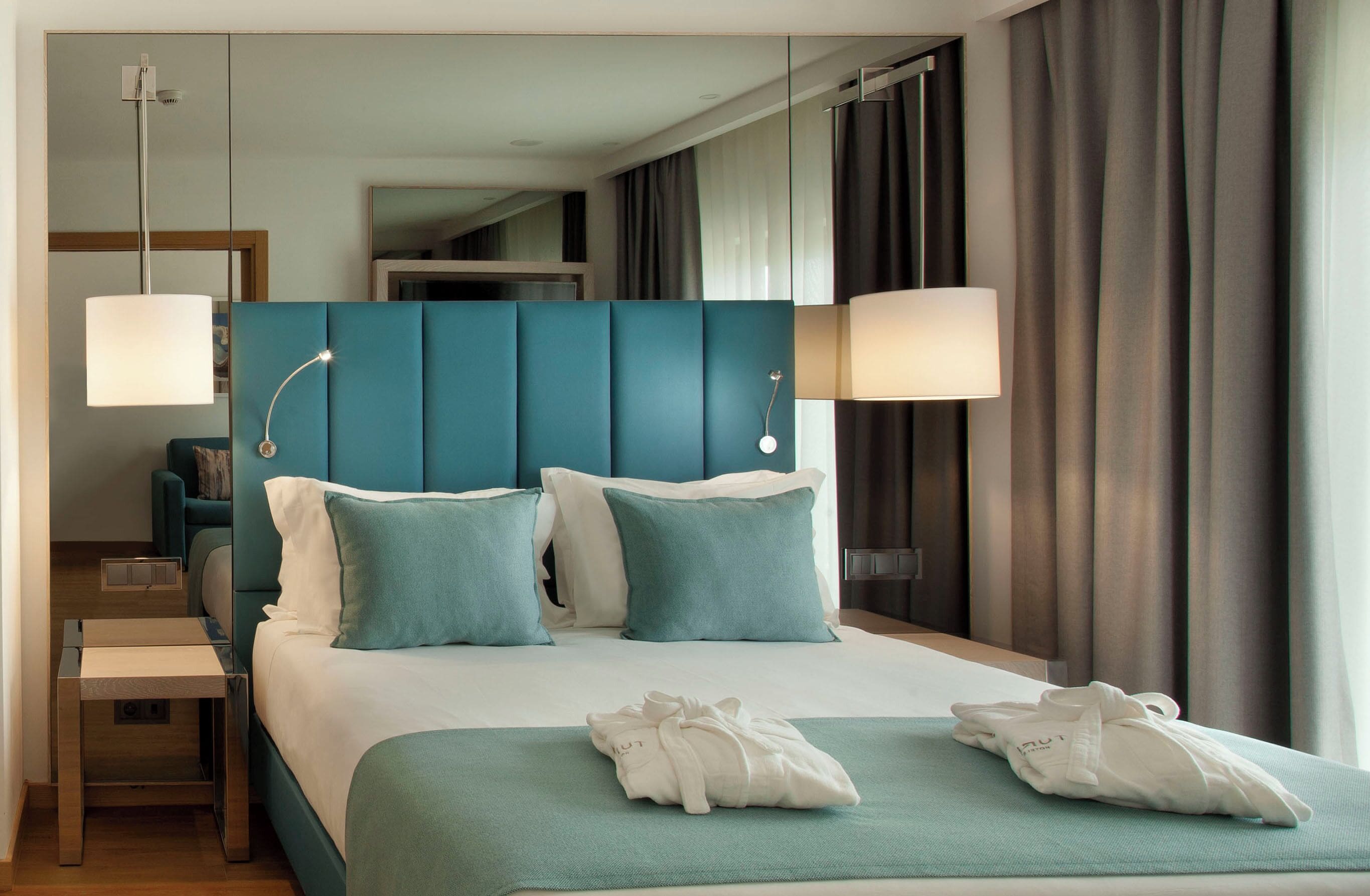 Habitación de hotel con una cama grande, dos lámparas de noche, una mesita de noche y vistas al pasillo.