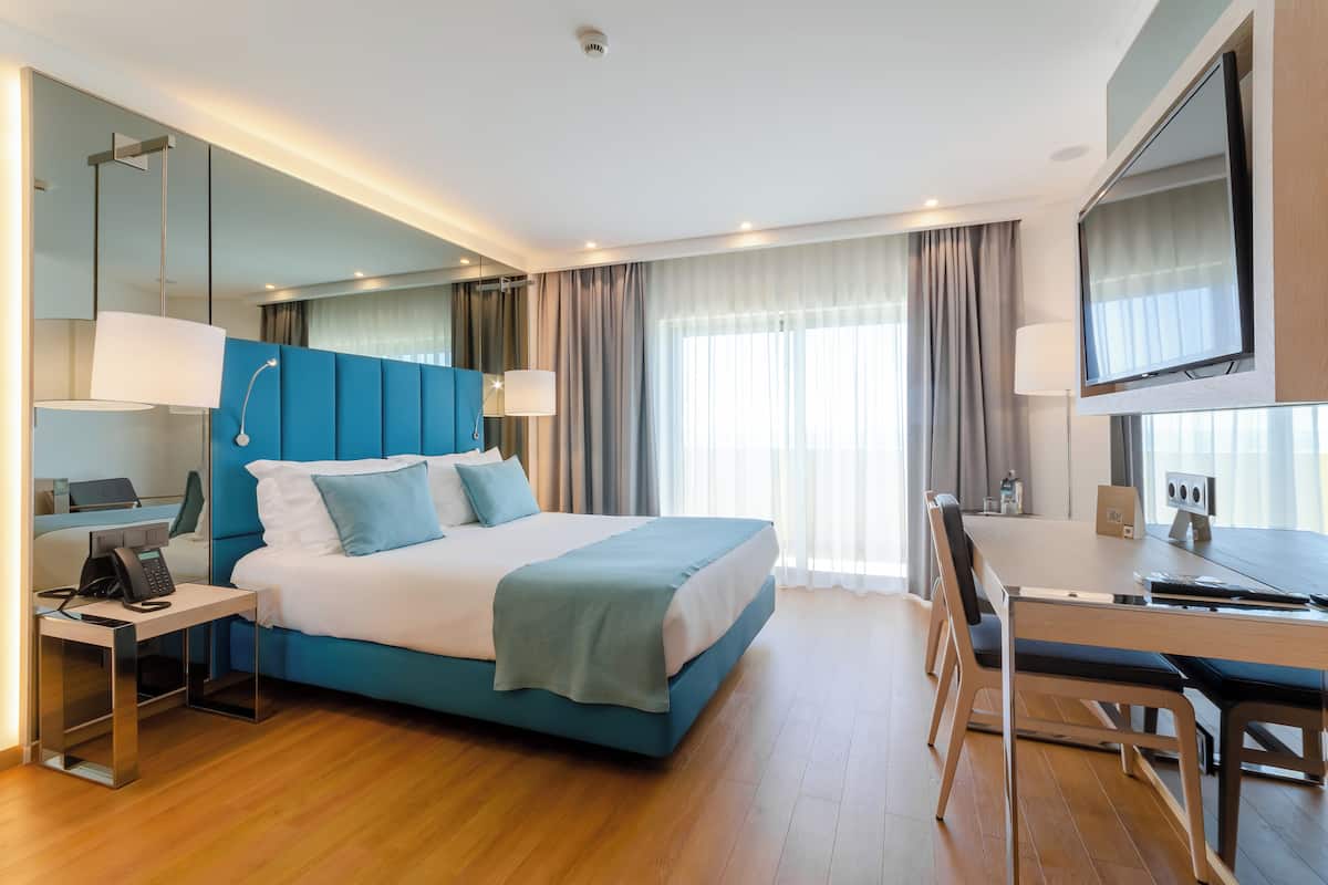 Quarto de hotel moderno com uma cama grande, uma escrivaninha e uma televisão.