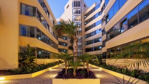 Een moderne hotelbinnenplaats met meerdere verdiepingen, grote ramen en een centrale palmboom omringd door planten.
