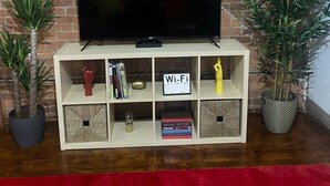 Un televisor de pantalla plana sobre un mueble de madera con un letrero de Wi-Fi, rodeado de libros y objetos decorativos, frente a una pared de ladrillo.