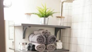A bathroom with a towel rack holding rolled towels and a potted plant.