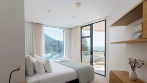Ein modernes Schlafzimmer mit einem großen Bett, einem Nachttisch, einer Kommode aus Holz und Blick auf einen Balkon mit einer schönen Landschaft.
