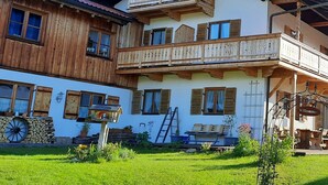 A two-story chalet with wooden balconies, a stone wall, and a welcoming sign.