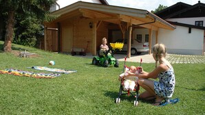 A grassy area with a wooden structure, a green toy tractor, and a child playing.