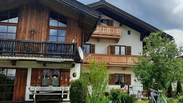A two-story wooden house with balconies, a satellite dish, and a bicycle in the yard.