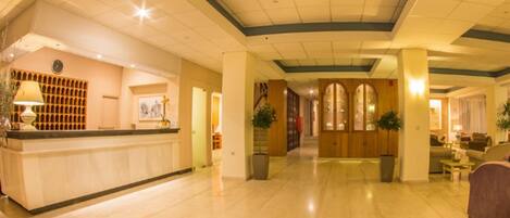 A spacious lobby with a reception desk, a large plant, and a seating area with a sofa and armchairs.
