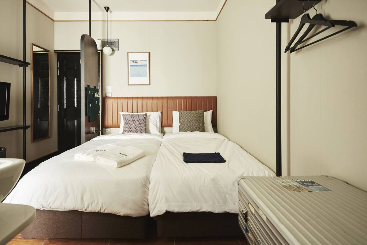 Ein Hotelzimmer mit zwei Betten, einem Schreibtisch, einem Stuhl, einem Spiegel, einem gerahmten Bild an der Wand und einer Lampe.