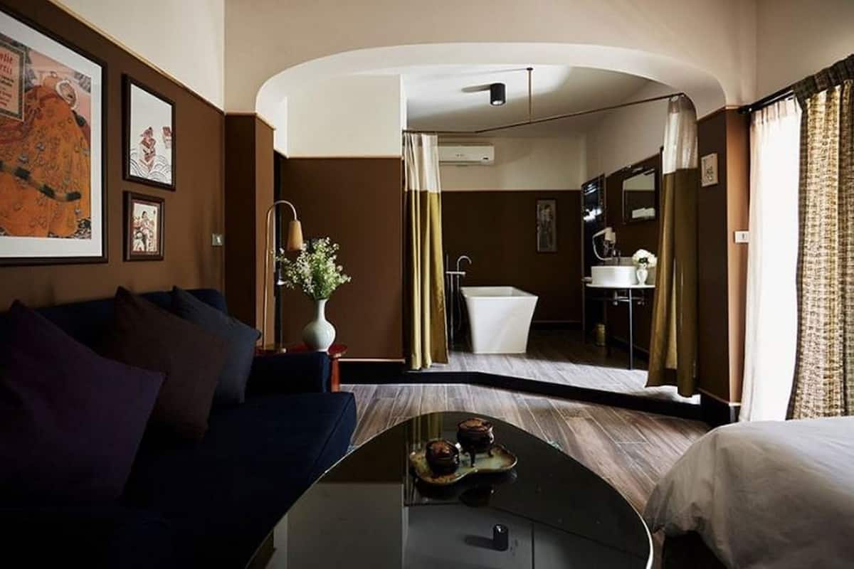 Ein Hotelzimmer mit einem bogenförmigen Bett, einer Sitzecke mit einer Couch, einem Badezimmer mit einer Badewanne und einem großen Spiegel, der den Raum reflektiert.