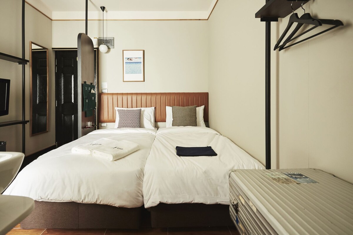 Habitación de hotel con dos camas, un escritorio, una silla, un espejo, un cuadro en la pared y una lámpara.