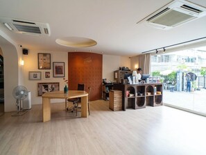 A hotel room with a wooden table, chairs, a desk with a computer, and a large window offering a view of the city. - Josh Hotel (Bangkok)