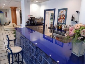 Een bar met een blauw aanrecht, barkrukken en een decoratieve vaas met bloemen.