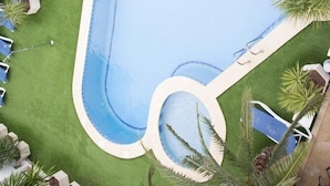 Vue aérienne d’une piscine entourée de chaises longues bleues et de palmiers.