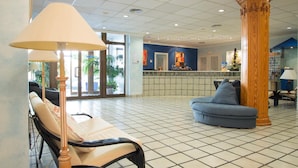 Un hall d’entrée avec un comptoir de réception, un fauteuil bleu, un canapé beige et une lampe.