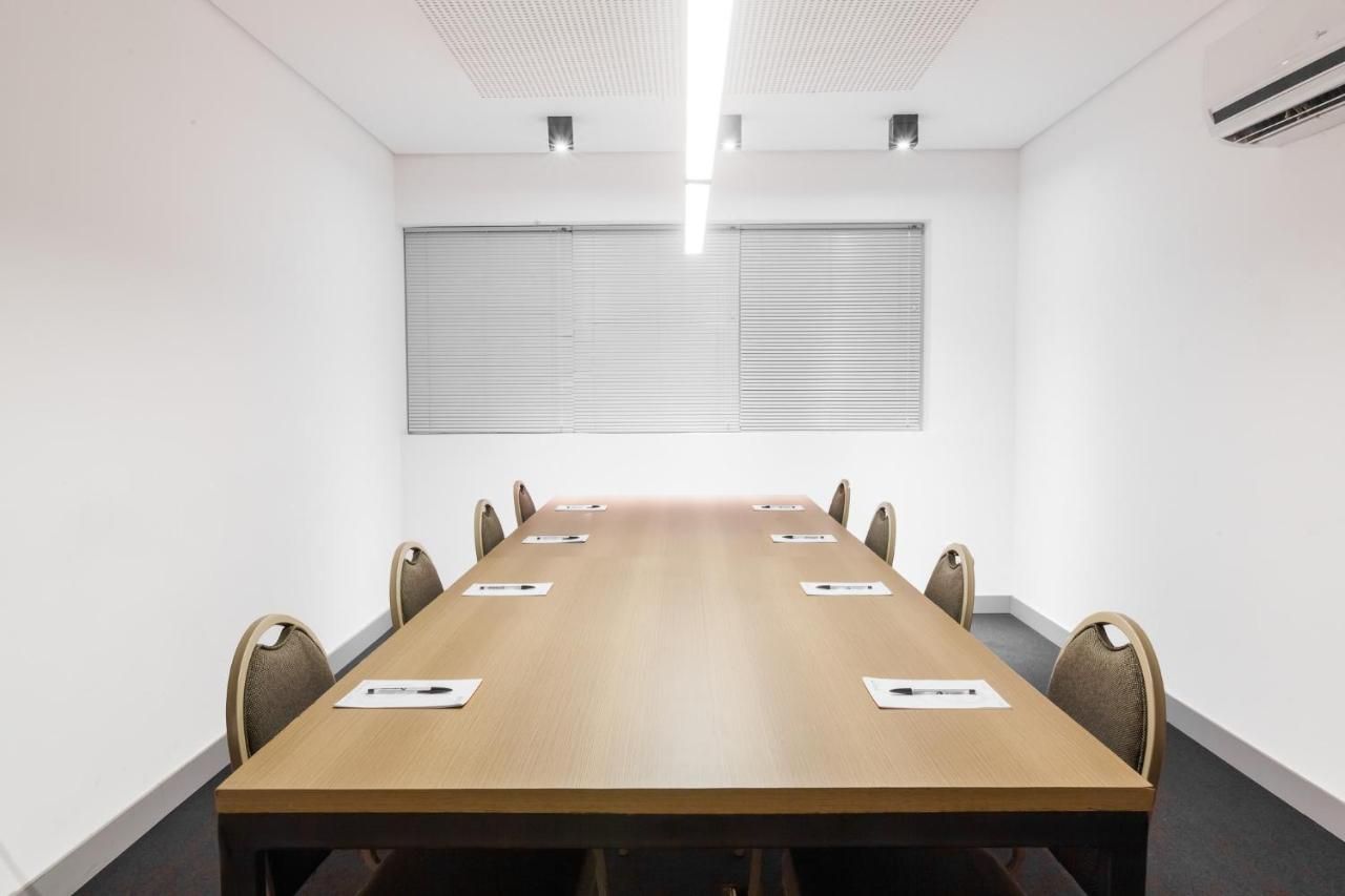 A conference room with a long table, chairs, and blinds on the windows.