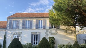 A two-story building with a tiled roof, multiple windows with shutters, and a well-maintained garden with trimmed hedges and a stone pathway.