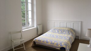 A bedroom with a bed, a window, a radiator, a chair, and a hanging light fixture.