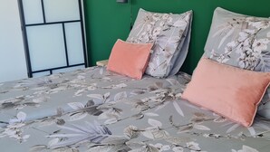 Una cama con ropa de cama floral, una pared verde y un ventanal con marco negro.