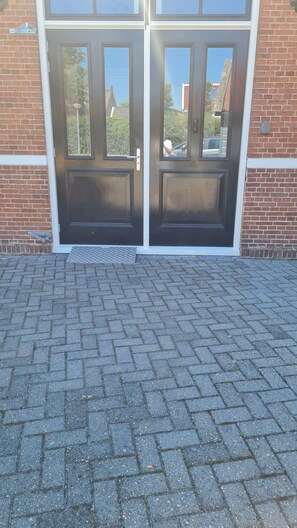A double door entrance with a metal kick plate, a brick wall, and a paved driveway. - Logement de 12e Stad - Private studio in former school near Leeuwarden (Berlikum)