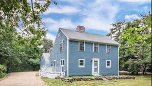 A two-story blue house with a front porch and stone foundation. - Charming Vineyard Saltbox + Ferry Tickets (Edgartown)