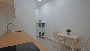 Una cucina moderna con piano di lavoro in legno e piano cottura a induzione, un tavolo da pranzo bianco con due sedie e un piccolo vaso con una pianta sul tavolo.