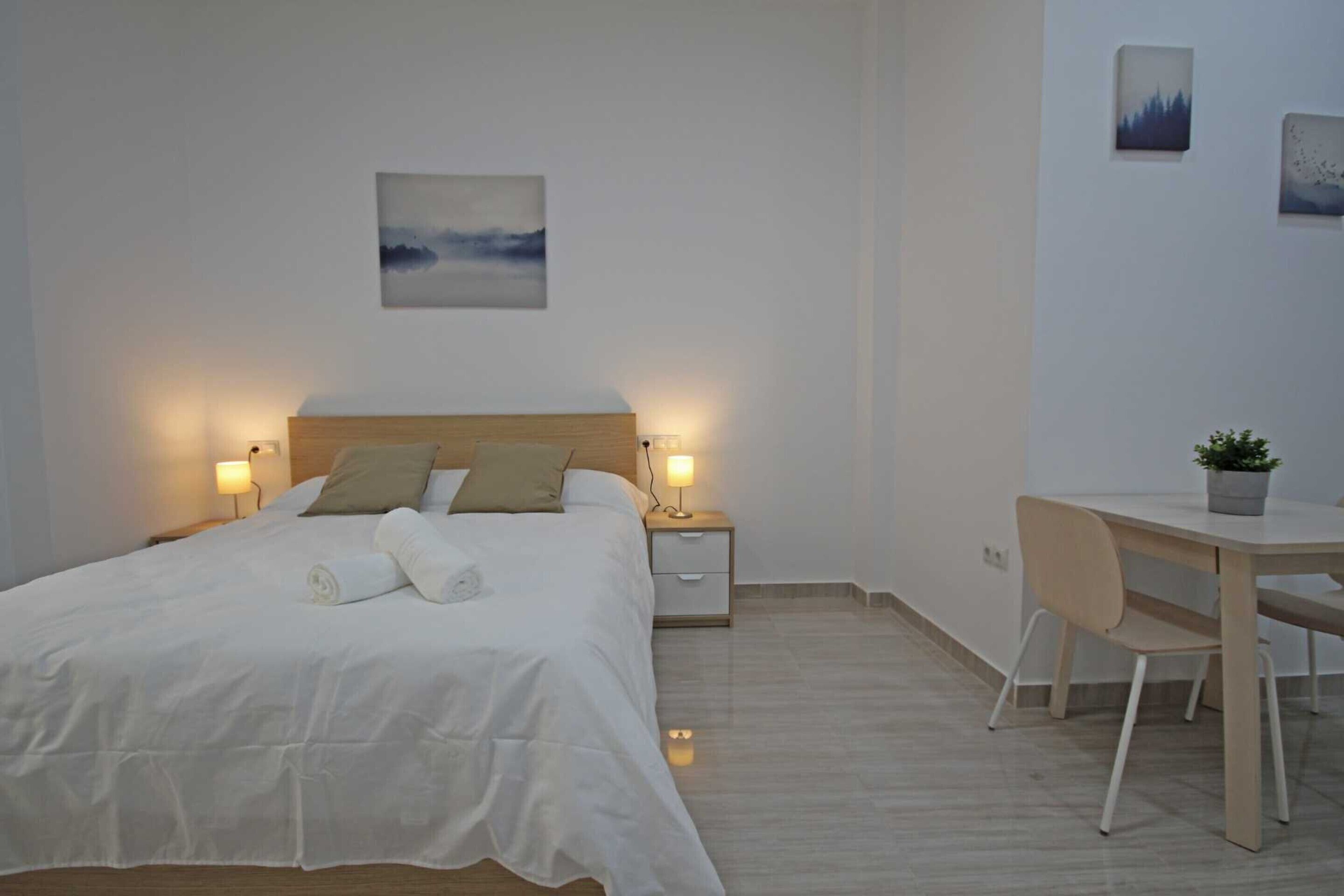 Une chambre bien rangée, avec un lit, des tables de chevet dotées de lampes, un bureau avec une chaise et une petite plante en pot.