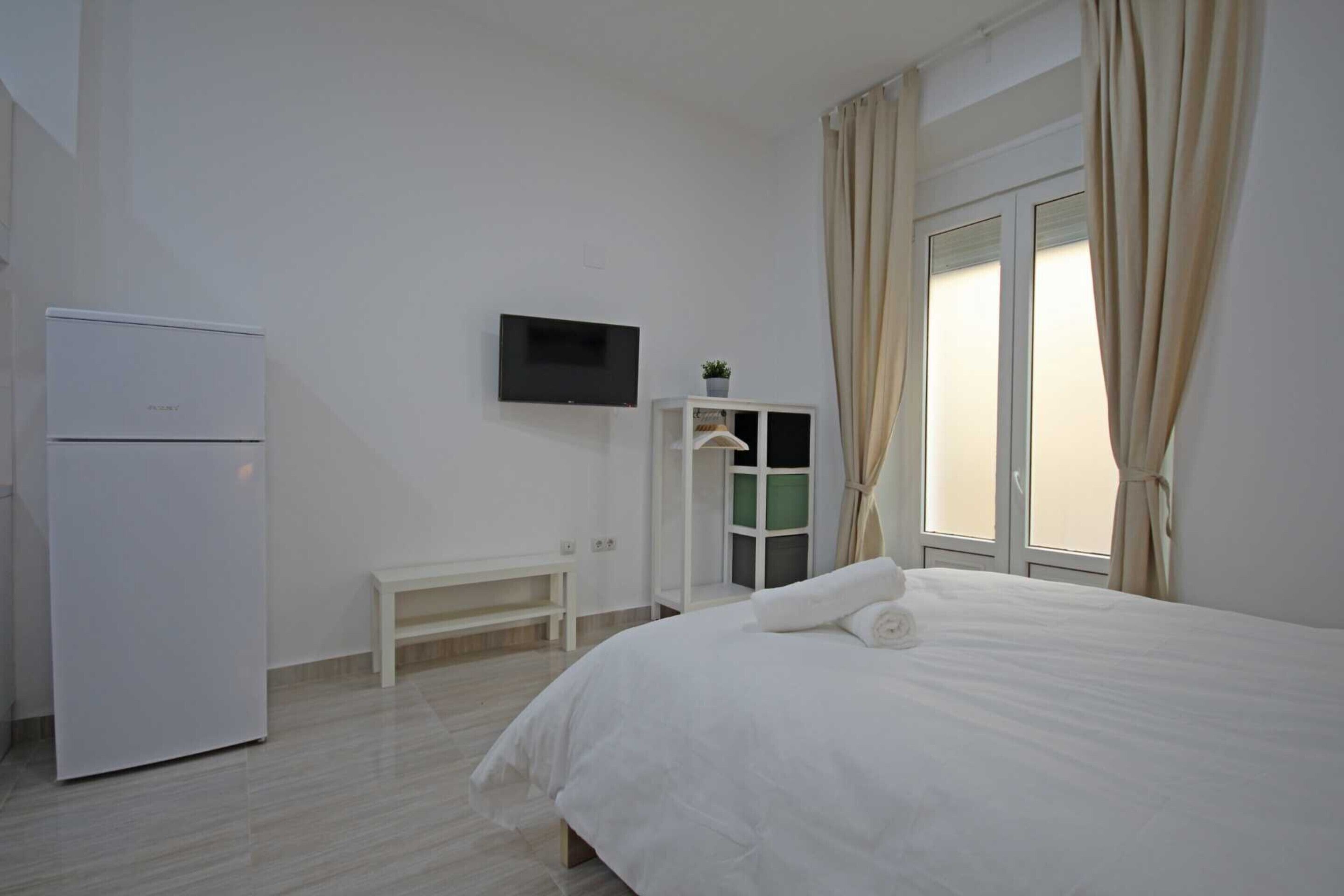 A hotel room with a bed, a TV mounted on the wall, a small table, and a window with curtains.