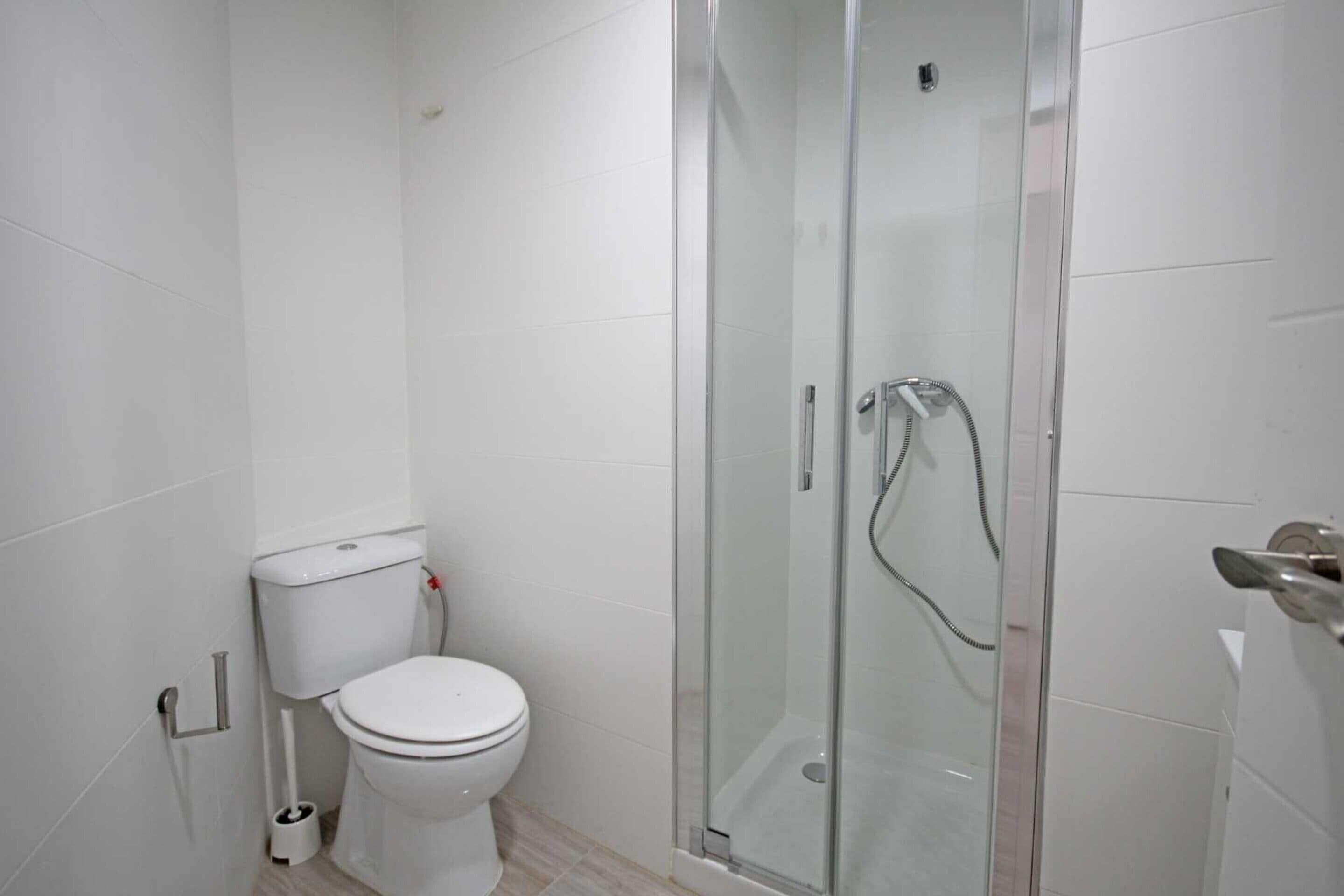 Un baño moderno con inodoro, ducha envuelta en vidrio y paredes cubiertas de azulejos blancos.