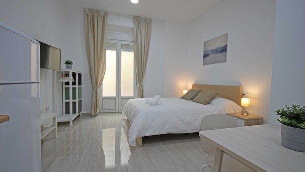Una camera d'albergo moderna con un letto, un comodino, una lampada e vista sull'esterno attraverso una finestra con tende.