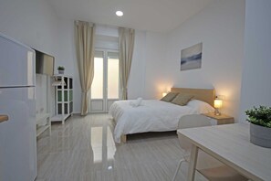 A modern hotel room with a bed, bedside table, lamp, and a view of the outdoors through a window with curtains. - Esparteros 6 Estudios  (Málaga)
