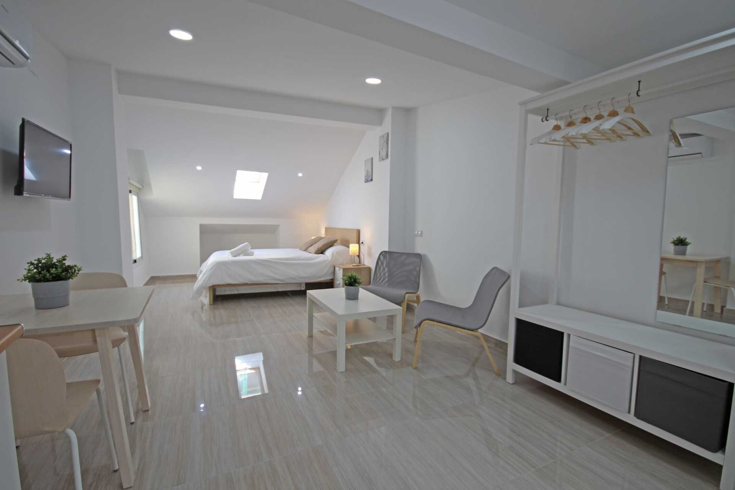 A modern, well-lit bedroom with a bed, bedside table, chair, and a large mirror.