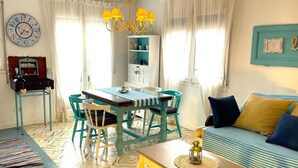 A cozy living room with a dining area, a teal sofa, and a wall clock.