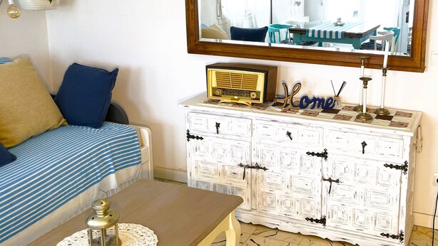 A cozy living room with a sofa, a coffee table, a vintage radio, and a large mirror above a white cabinet.