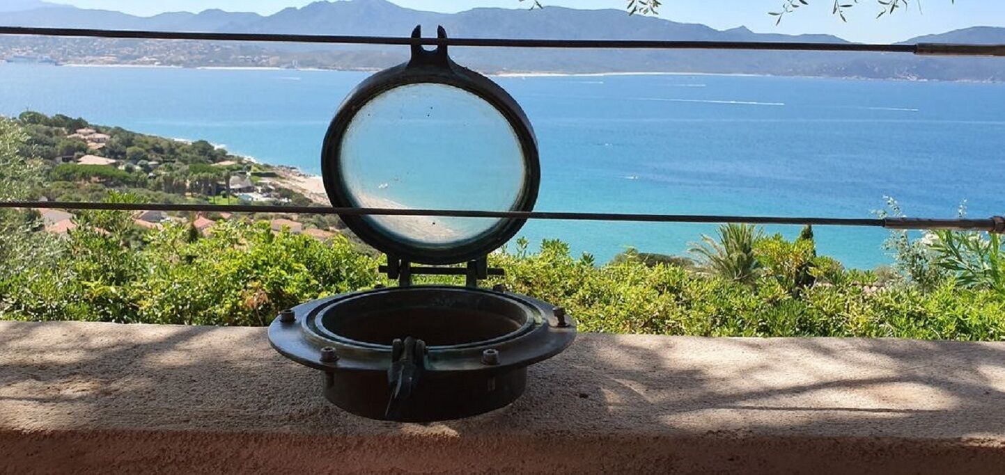 Uno specchio tondo su un supporto, con vista sul mare sullo sfondo.