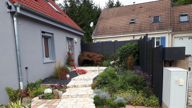A residential garden with a stone pathway leading to a house with a red-tiled roof. - Cozy gite 3 *, 2 to 4 people, 1st floor in the house. Individual entrance. (67370 Berstett)