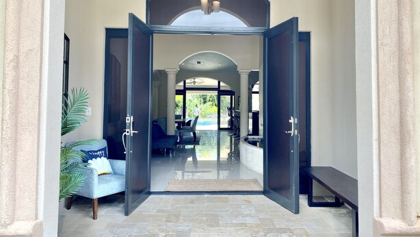 Entrada de hotel con puerta de cristal, un banco y vista al área de la piscina.