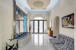 A modern lobby with a glass table, a grey sofa, a large abstract painting, and a water feature. - 144' New River Dock DT FTL! Sailfish Pool, Hottub, Pontoon & Fire Lounge Luxury! (Fort Lauderdale)